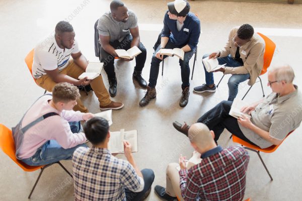 Men reading and discussing bible in prayer group circle.